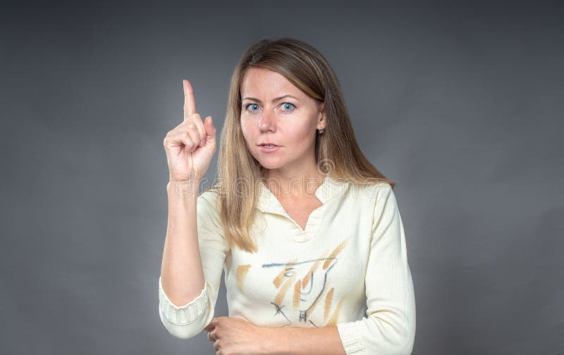 Portrait of woman with attention gesture. She holding finger up, warning listen to me be careful. Close up of girl