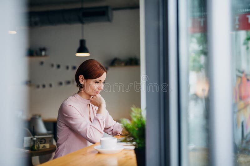 A portrait of attractive woman with coffee sitting at the table in a cafe, using laptop.