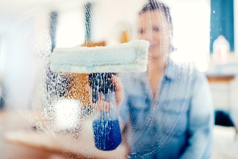 Portrait of woman doing housekeeping works. Young woman using window cleaner and doing chores around the house stock photos
