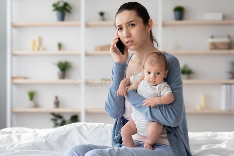 Worry Young Mother Holding Newborn Baby On hands And Talking On Cellphone