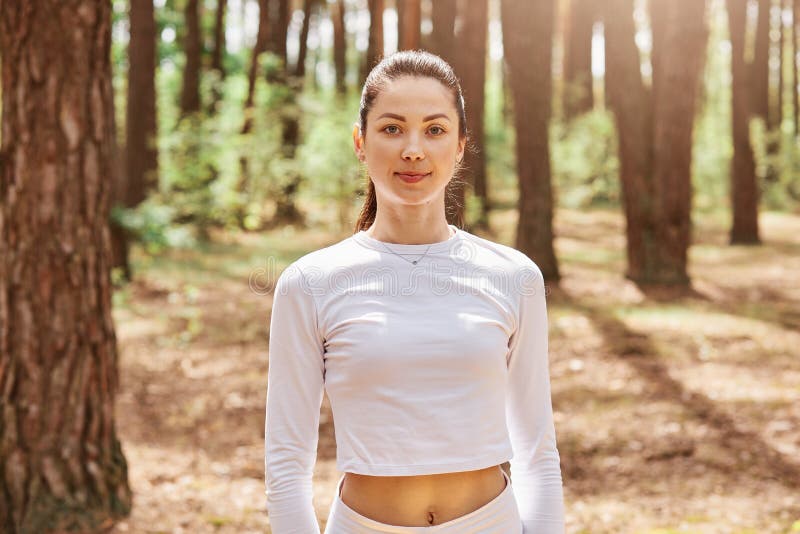 Portrait of young adult attractive dark haired female in stylish sportswear posing in forest before or after training, expression