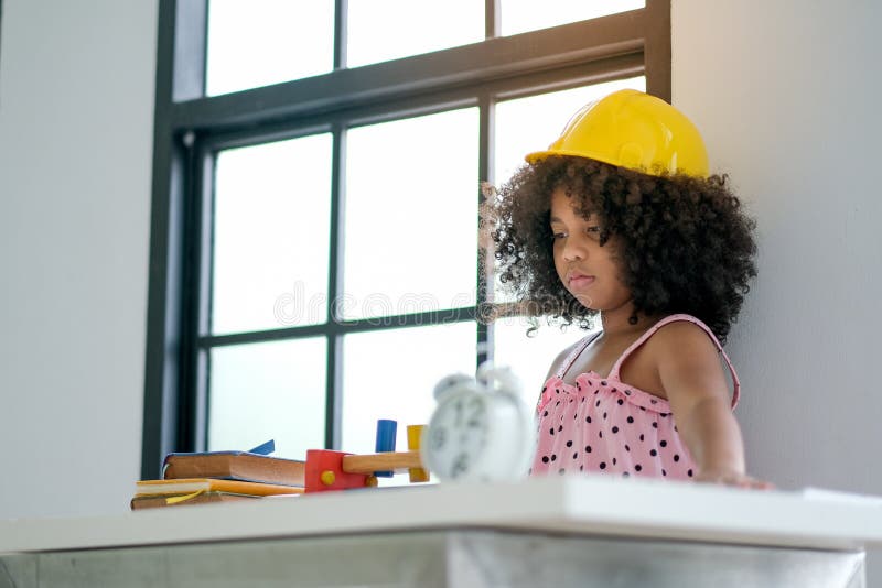 Portrait of young African girl play as engineer by wearing yellow hat in the living room with some decorations stock photos