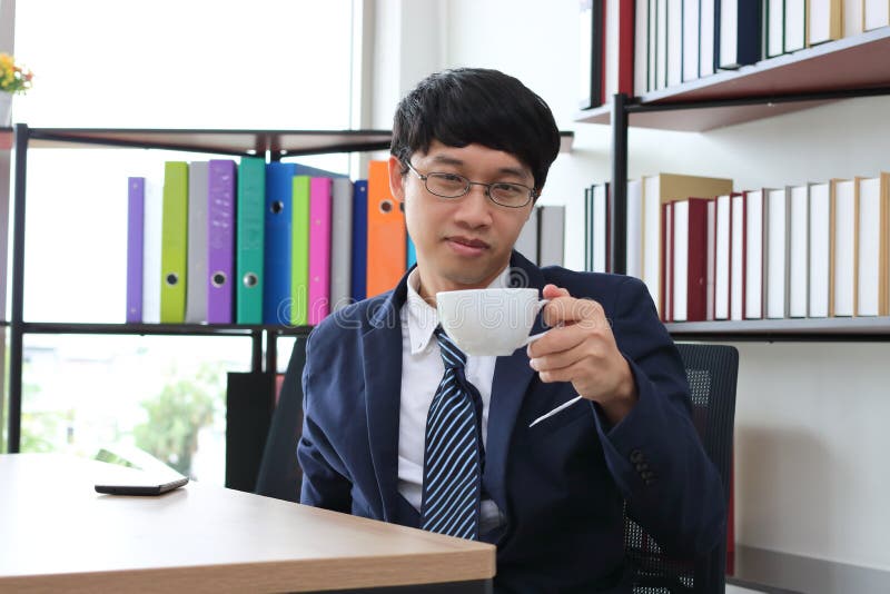 Portrait of young Asian business man in formal suit drinking coffee in office stock photos Portrait of young Asian business man in formal suit drinking coffee in office stock photos
