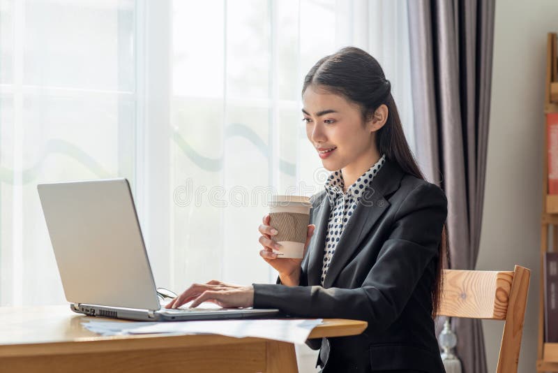 Portrait of Young Asian business woman drinking coffee and using her laptop in her office