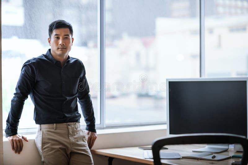 Confident young Asian businessman standing by windows in an office