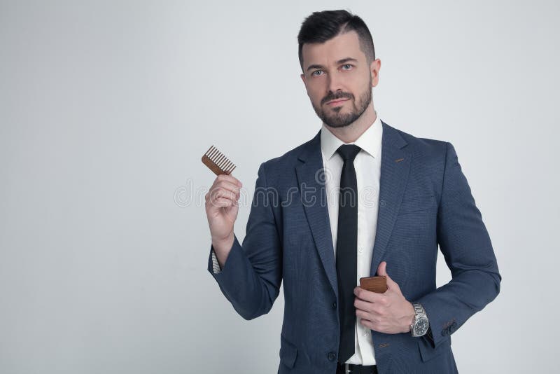 Portrait of young attractive businessman with serious and confident look, holding wooden comb. Stylish bearded barber in suit stock photo Portrait of young attractive businessman with serious and confident look, holding wooden comb. Stylish bearded barber in suit stock photo