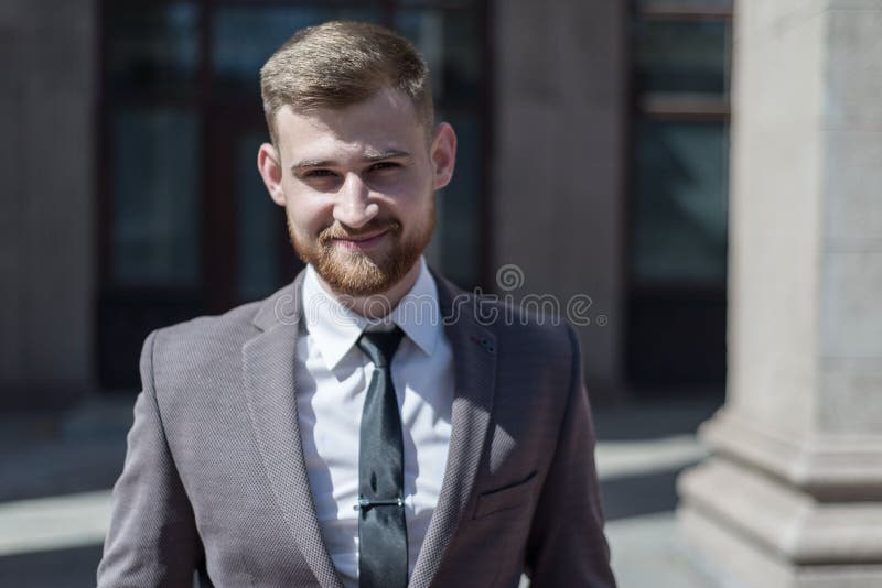Portrait of a young bearded guy of twenty-five years old, in a business suit, against the background of an office building. Posing