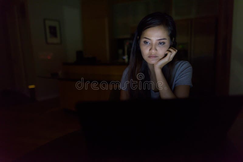 Young beautiful Asian woman using laptop in the dark living room