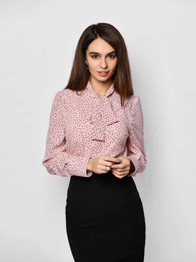 Portrait of young beautiful brunette woman in business formal pink blouse shirt and black skirt on grey wall background