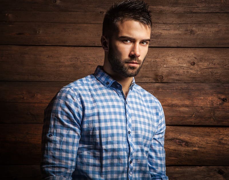 Portrait of young beautiful fashionable man against wooden wall.