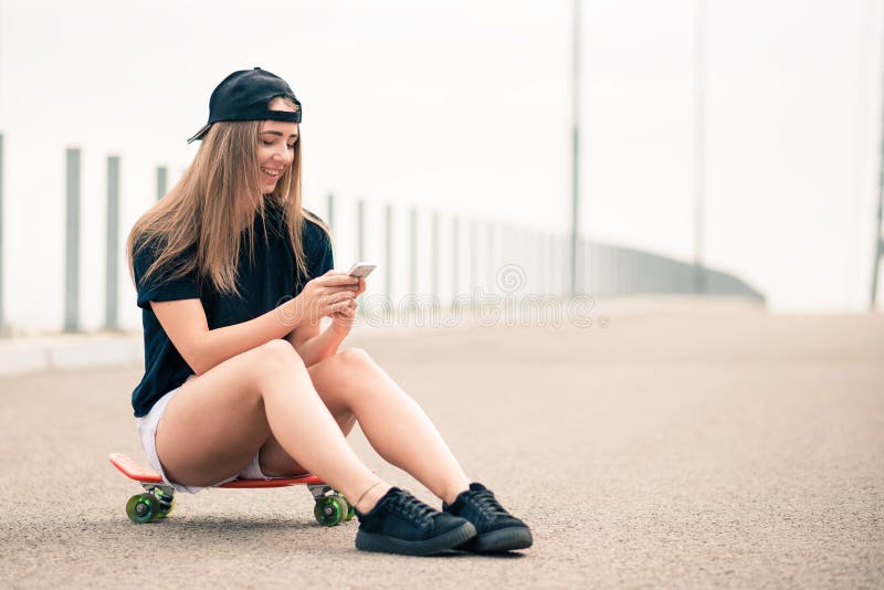 Young Beautiful Smiling Blonde Girl Using Smartphone while Sitting on the Skateboard royalty free stock image Young Beautiful Smiling Blonde Girl Using Smartphone while Sitting on the Skateboard royalty free stock image