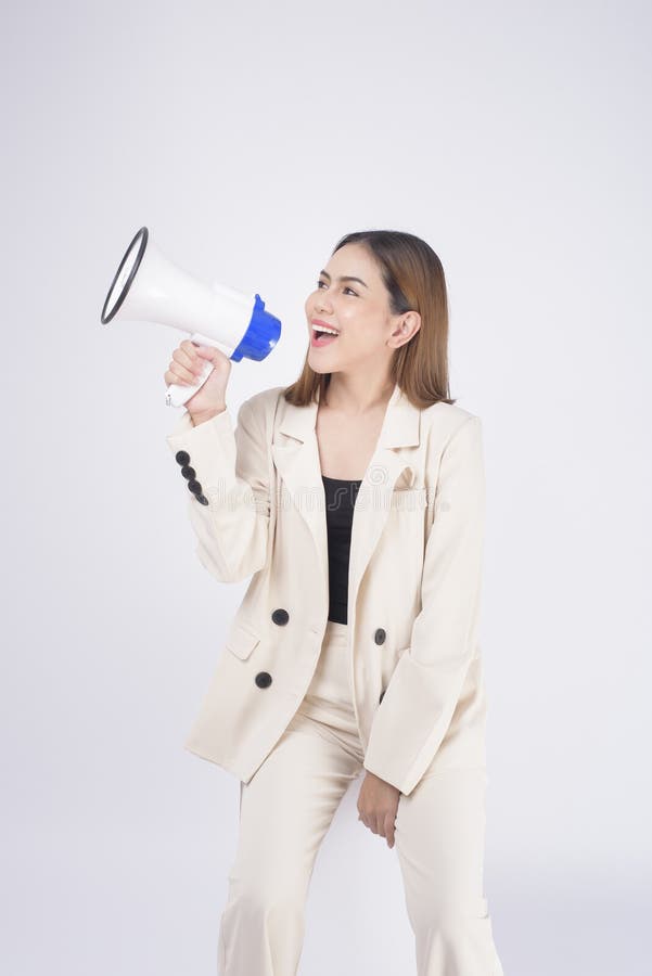 A portrait of young beautiful smiling woman in suit using megaphone to announce over isolated white background studio