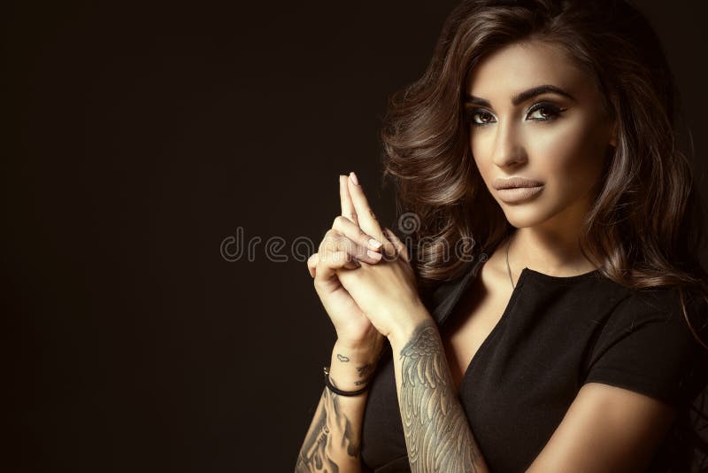 Portrait of young beautiful tattooed woman with luxuriant shining wavy hair and perfect make up holding hands in shooting gesture royalty free stock photo Portrait of young beautiful tattooed woman with luxuriant shining wavy hair and perfect make up holding hands in shooting gesture royalty free stock photo