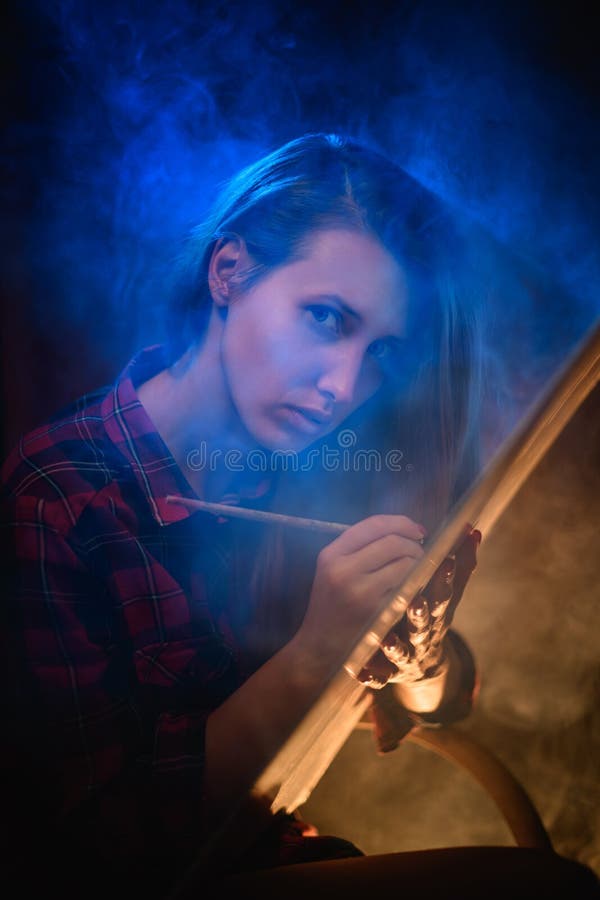 Portrait of young beautiful woman with long hair who paints with brush on canvas. Smoke around.