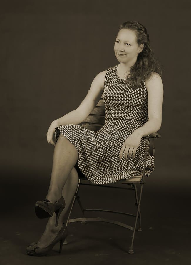 Portrait of young beautiful woman sitting on an old metal with wooden chair. She is wearing a dress, bare arms and has curly brown