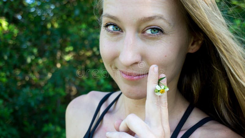 Cute portrait of young blonde woman face smoking daisy flower weed smiling with blue clear eyes isolated in nature