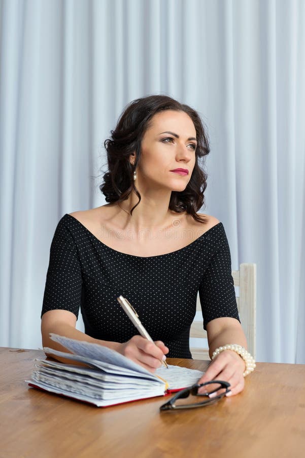 Portrait of a young business woman coach sitting at the teacher`s desk with a notebook and pen and looking out the window
