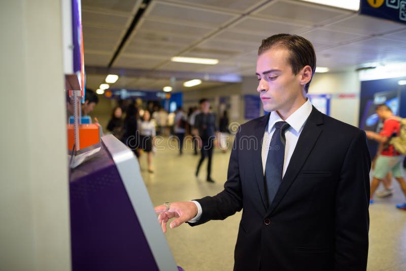 Young businessman using ATM machine at train station stock photos Young businessman using ATM machine at train station stock photos