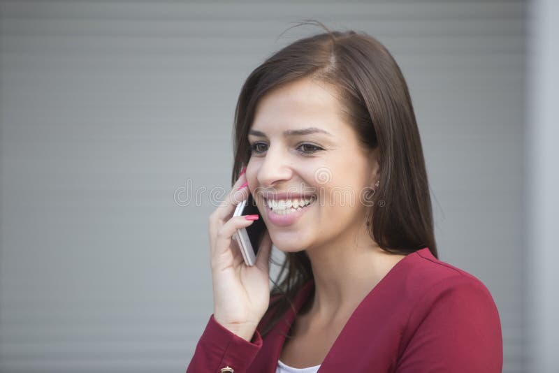 Young businesswoman in red blazer talking over the mobile phone. Portrait of young businesswoman in red blazer talking over the mobile phone in front of office stock image Young businesswoman in red blazer talking over the mobile phone. Portrait of young businesswoman in red blazer talking over the mobile phone in front of office stock image