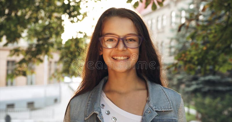 Portrait of the young child. Little girl in purple eyeglasses is smiling at camera in sun flares. 4k footage.