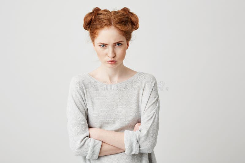 Portrait of young cute foxy offended girl with buns looking at camera with crossed arms over white background.