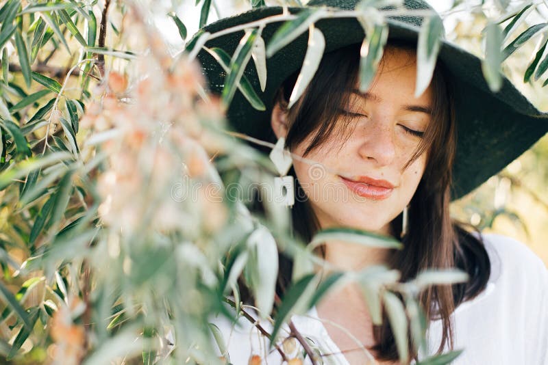 Portrait of young fashionable woman with modern earrings posing in green olive branches in soft evening light, stylish boho girl royalty free stock photo Portrait of young fashionable woman with modern earrings posing in green olive branches in soft evening light, stylish boho girl royalty free stock photo