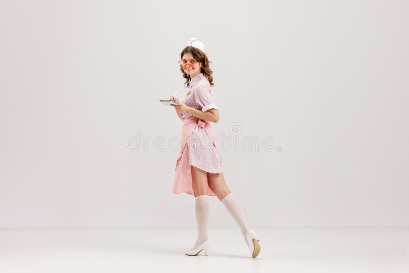 Portrait of young female waitress, sensual woman in retro american fashion style of 70s, 80s in action motion over grey