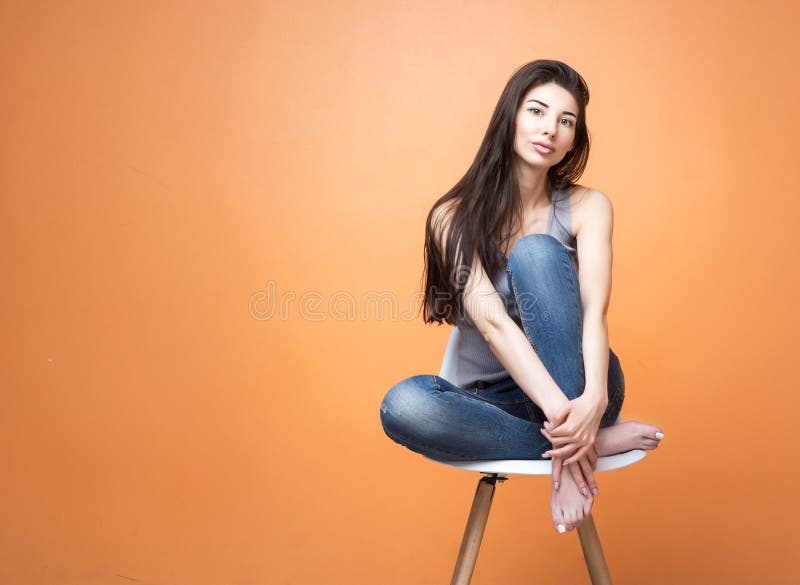 Portrait of a young girl sitting in the chair and looking into the camera against orange background. Lifestyle and people concept royalty free stock photos Portrait of a young girl sitting in the chair and looking into the camera against orange background. Lifestyle and people concept royalty free stock photos