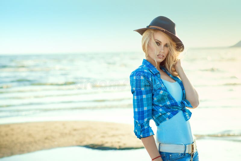 Portrait of young gorgeous blond in blue checked shirt and hat standing at the seaside, her hair blown by the wind stock photo Portrait of young gorgeous blond in blue checked shirt and hat standing at the seaside, her hair blown by the wind stock photo