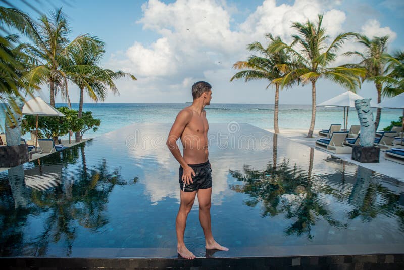 Portrait of young handsome man model standing on on the edge of swimming pool at the tropical island luxury resort stock image Portrait of young handsome man model standing on on the edge of swimming pool at the tropical island luxury resort stock image