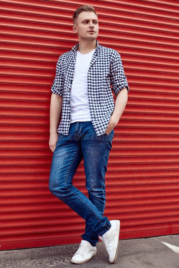 Young handsome man in a shirt and jeans near the red gate