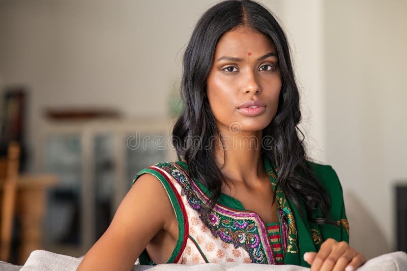 Portrait of young and attractive Indian woman in a white top sitting in a  wood chair and smiling radiantly Stock Photo