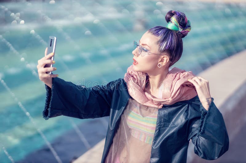 Portrait of a young lady with crazy look taking self-portraits selfie. Urban outdoor with fountains in background. Model girl stock photography Portrait of a young lady with crazy look taking self-portraits selfie. Urban outdoor with fountains in background. Model girl stock photography