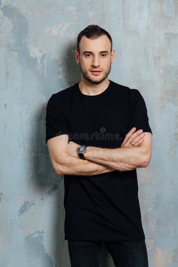 Portrait of a young man in a black T-shirt leaned against a vintage gray wall. Copy space.