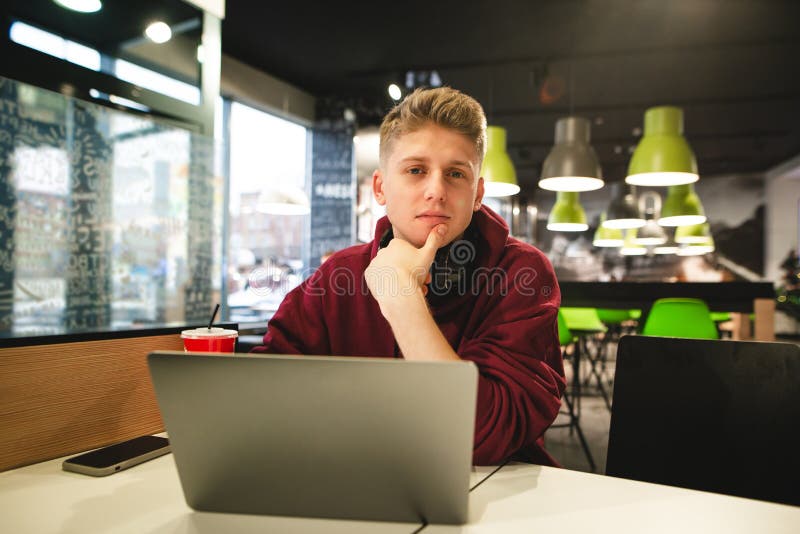 Portrait of a young man in casual clothing sitting with a laptop in a fast food cafe, looking at the camera royalty free stock images Portrait of a young man in casual clothing sitting with a laptop in a fast food cafe, looking at the camera royalty free stock images