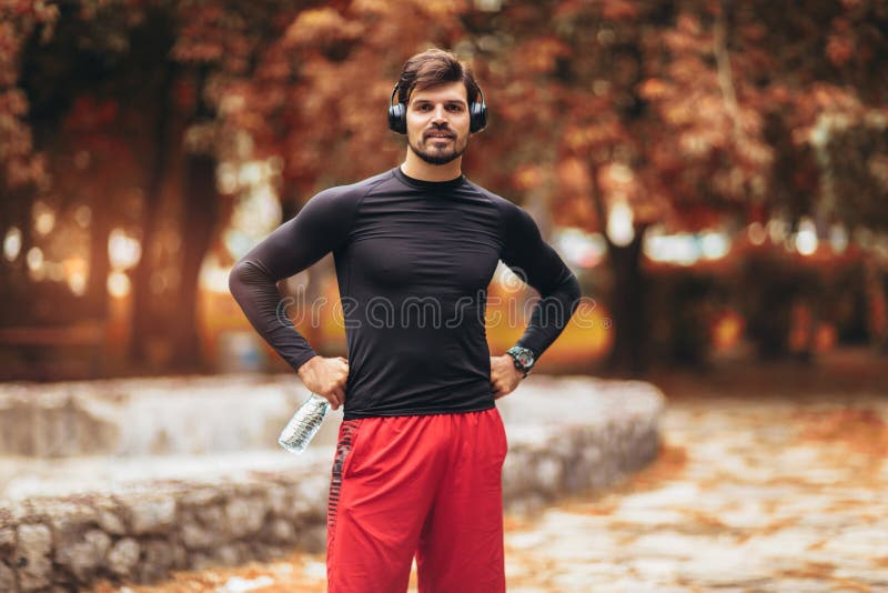 Young man on a morning jogging in the autumn park, man listening to music with headphones