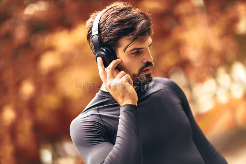 Young man on a morning jogging in the autumn park, man listening to music with headphones