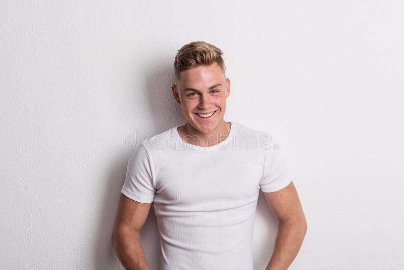 Portrait of a young man in white T-shirt in a studio, leaning against wall.