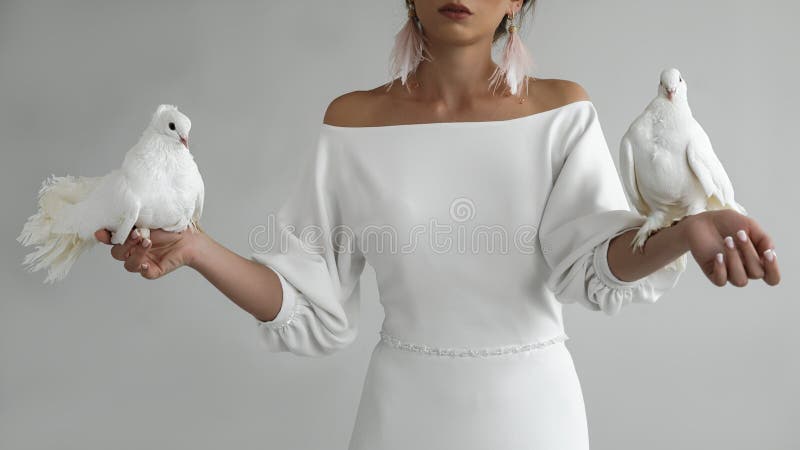 Portrait of a young newlywed young bride in a beautiful white dress with a cleavage, holding two white doves in her hands