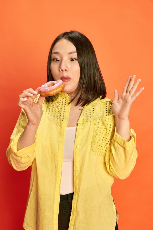 Portrait Of Young Pretty Asian Girl In Yellow Blouse Holding Pink Donut Posing Against 