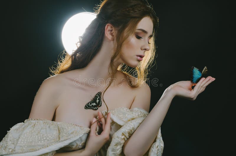 Portrait of a young red-haired woman in a vintage ash dress with open back and shoulders in the moonlight on a black background. S