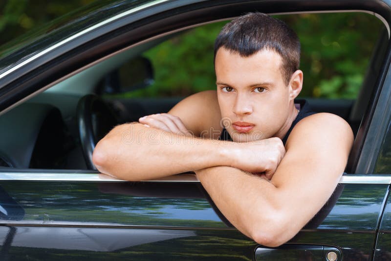 Portrait young serious man sits car looks open window background summer green park. Portrait young serious man sits car looks open window background summer green park