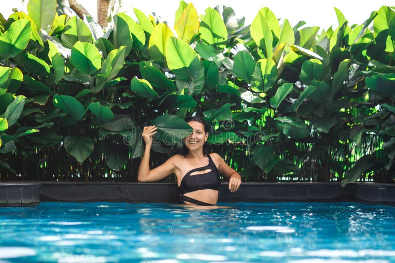 Portrait of young sexy caucasian woman in swimming pool with green plants