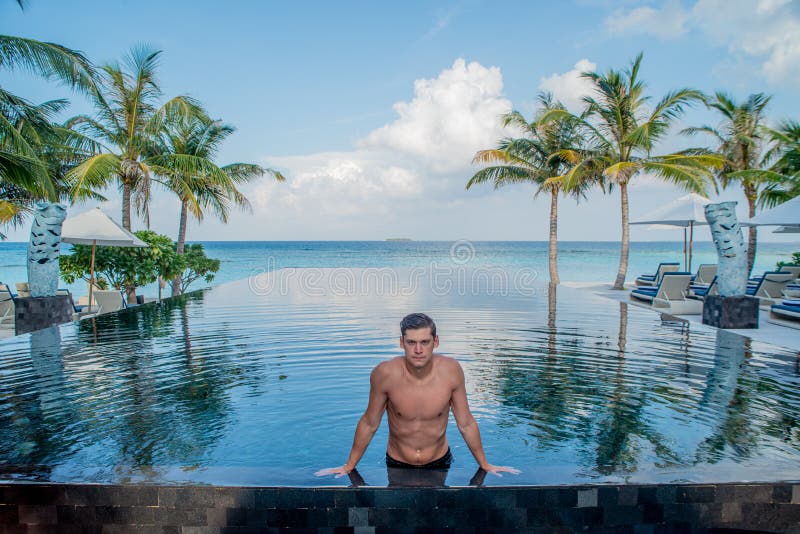 Portrait of young sexy handsome man model resting at the edge of the swimming pool at the tropical island luxury resort royalty free stock photos Portrait of young sexy handsome man model resting at the edge of the swimming pool at the tropical island luxury resort royalty free stock photos