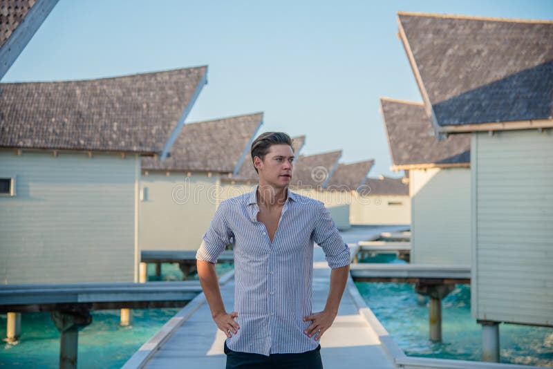 Portrait of young sexy male model posing in expensive shirt sitting on the swing at the tropical island luxury resort stock images Portrait of young sexy male model posing in expensive shirt sitting on the swing at the tropical island luxury resort stock images