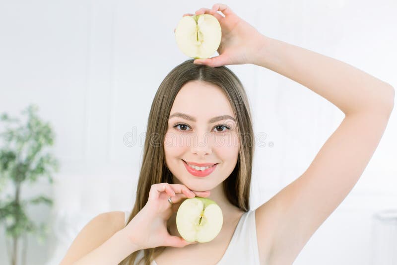 Portrait of a young smiling beautiful girl with two halves of apples in her hands, above and below the face. Pretty