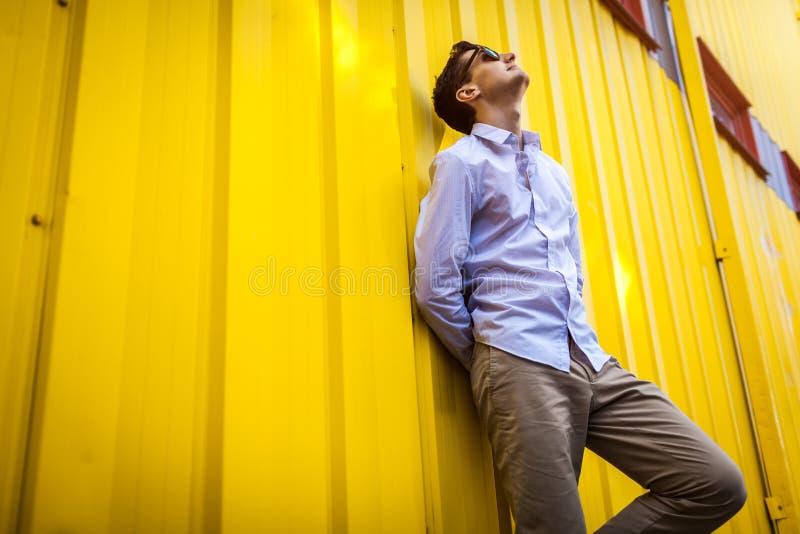 Portrait of young stylish man standing against yellow wall outdoors. Summer fashionable outfit. royalty free stock images Portrait of young stylish man standing against yellow wall outdoors. Summer fashionable outfit. royalty free stock images