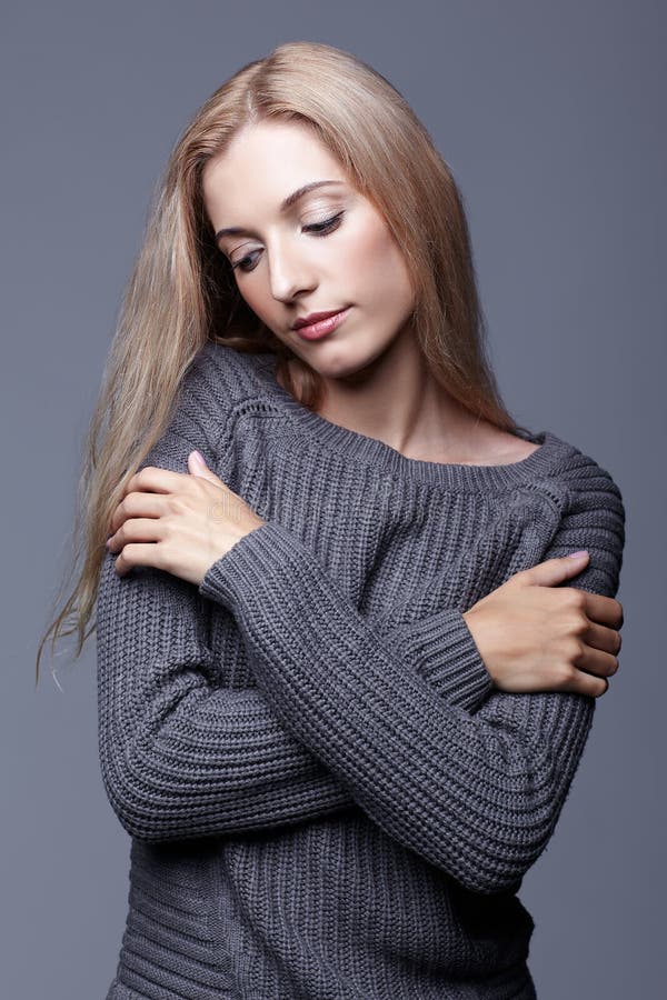 Portrait of young woman in gray woolen sweater with hands crossed. Beautiful girl posing on grey studio background. Female with b stock image Portrait of young woman in gray woolen sweater with hands crossed. Beautiful girl posing on grey studio background. Female with b stock image