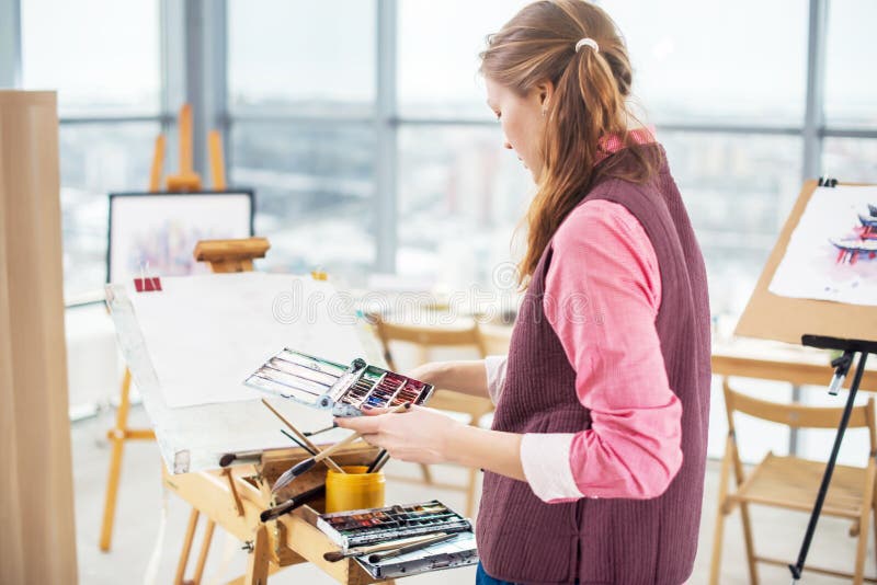 Portrait of a young woman painter drawing with watercolor palette on paper using easel. stock photos Portrait of a young woman painter drawing with watercolor palette on paper using easel. stock photos