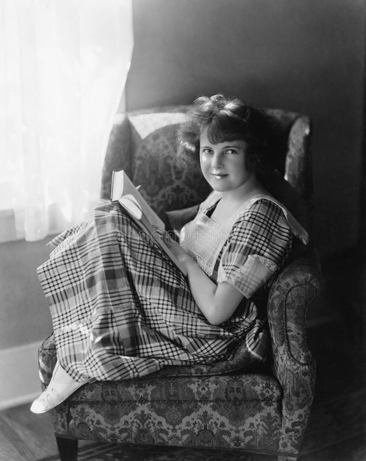 Portrait of a young woman sitting in an armchair and holding a book stock photo Portrait of a young woman sitting in an armchair and holding a book stock photo